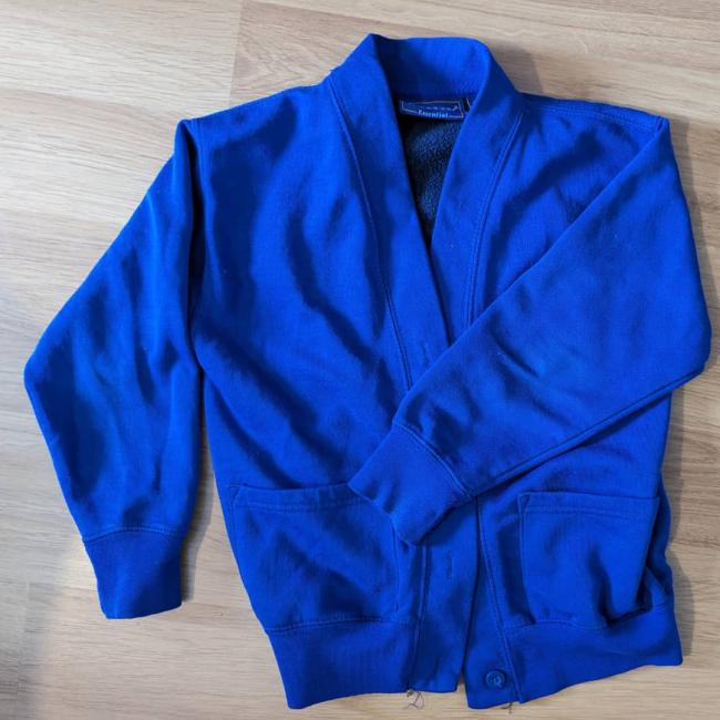A blue school cardigan jumper placed on a laminated floor 