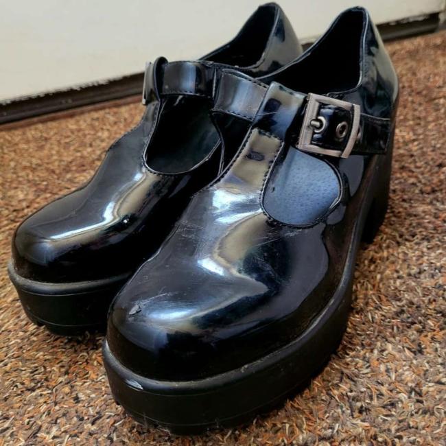 Black patent school shoes placed on some brown patterned carpet. 