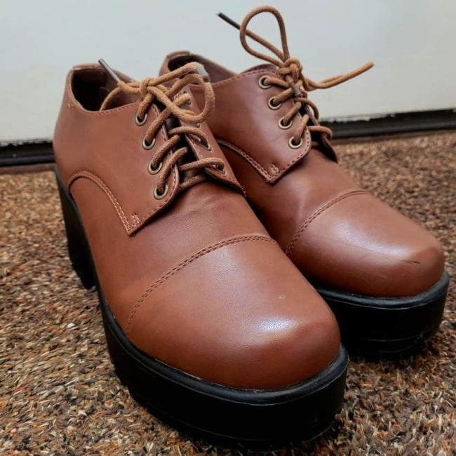 Brown school shoes placed on some brown patterned carpet 