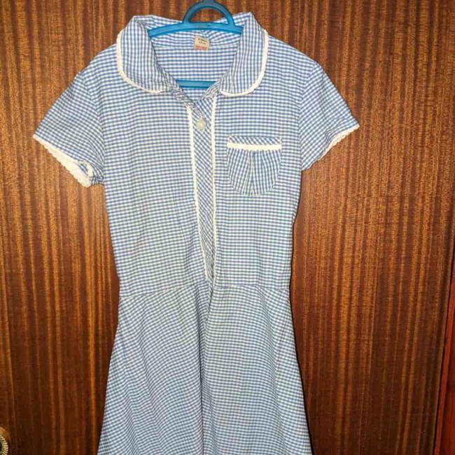 A blue striped girls school uniform hanging on the back of a wooden door 