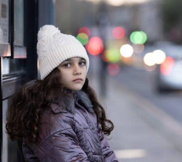 Young girl wearing white hat and winter coat sat at a bus stop