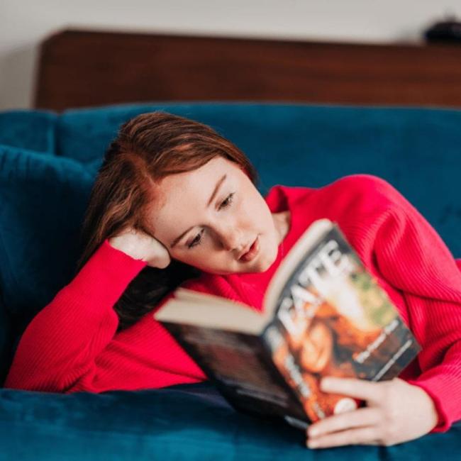 A teenage girl reading a book on a blue sofa