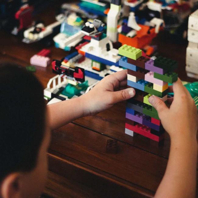 A young boy playing with lego on a wooden table.
