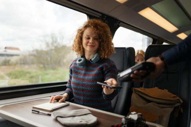 An image of a young person on a train getting her ticket scanned by the inspector