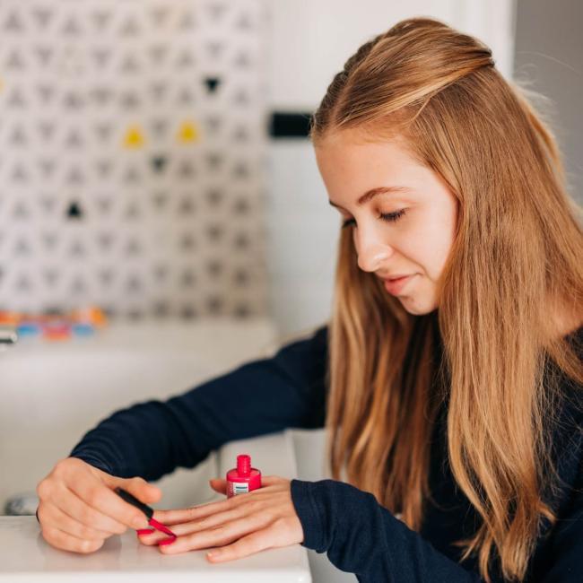 A teenage girl painting her nails red on a porcelain sink