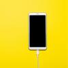A mobile phone on charge placed on a yellow background