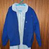 A blue checked girls school dress with a blue jumper on top, hanging on the back of a wooden door
