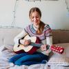 A teenage girl playing a guitar on her bed