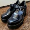 Black patent school shoes placed on some brown patterned carpet.